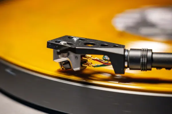 Aguja de tocadiscos apoyada sobre el surco de un disco de vinilo ámbar, con la cápsula y el portacápsulas en primer plano