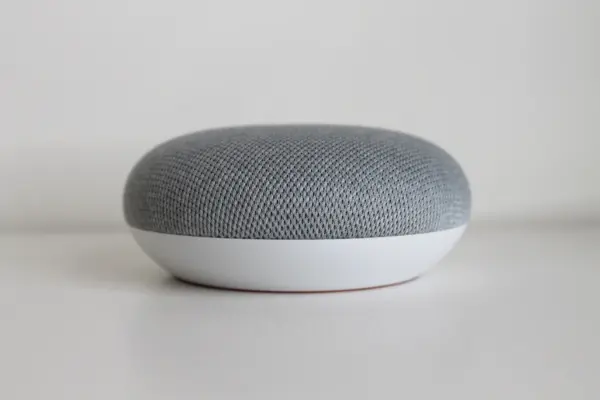 Altavoz inteligente compacto recubierto de tela gris sobre una superficie blanca con fondo neutro
