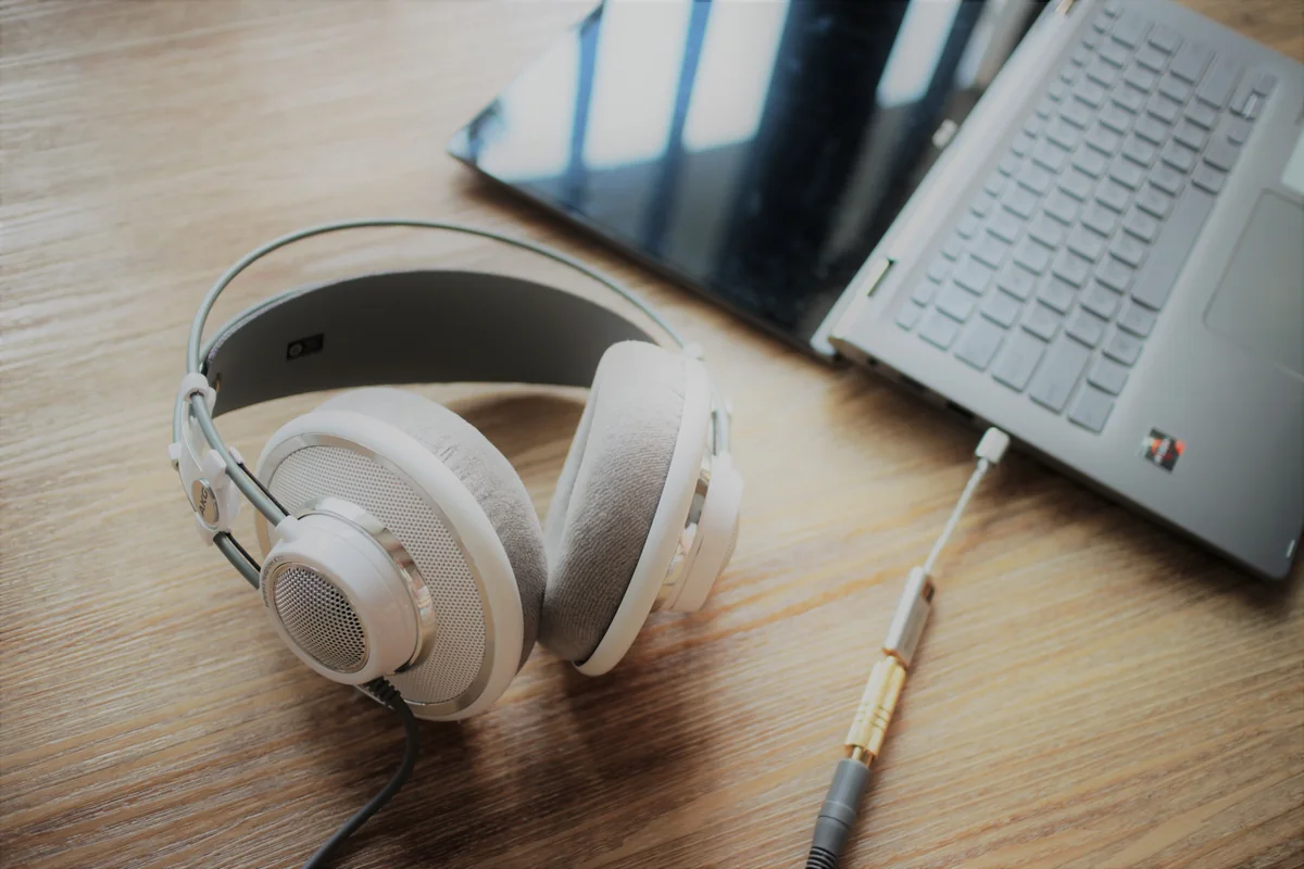 Auriculares over-ear con cable y adaptador conectados a un portatil sobre un escritorio de madera