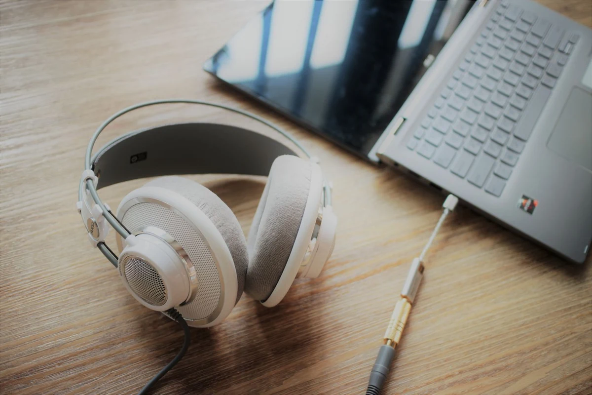 Auriculares de diadema abiertos conectados por cable a un DAC USB enchufado a un portátil sobre una mesa de madera