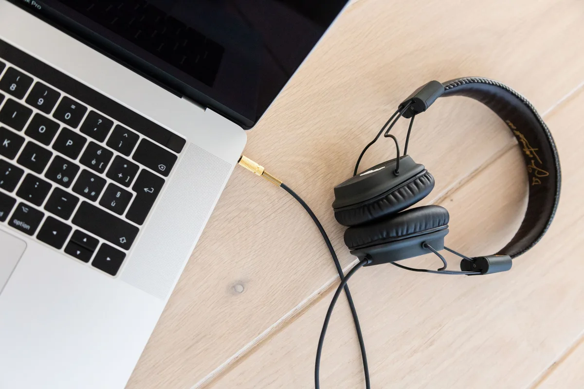 Auriculares de diadema con cable conectados a un portatil sobre un escritorio claro