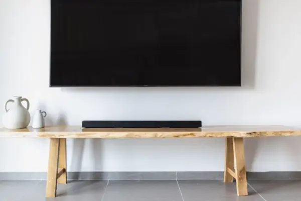 Barra de sonido negra sobre una consola de madera bajo un televisor de pared