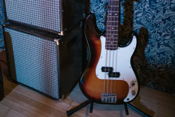Cuerpo de un bajo eléctrico de cuatro cuerdas sobre su soporte, con la pastilla y el puente en primer plano, junto a los altavoces de un amplificador