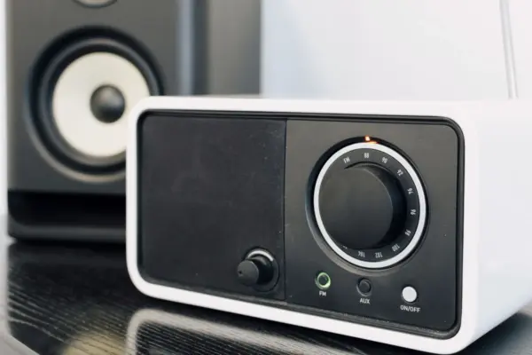 Equipo de musica compacto con dial de radio y un altavoz de estanteria detras, sobre un mueble de madera oscura