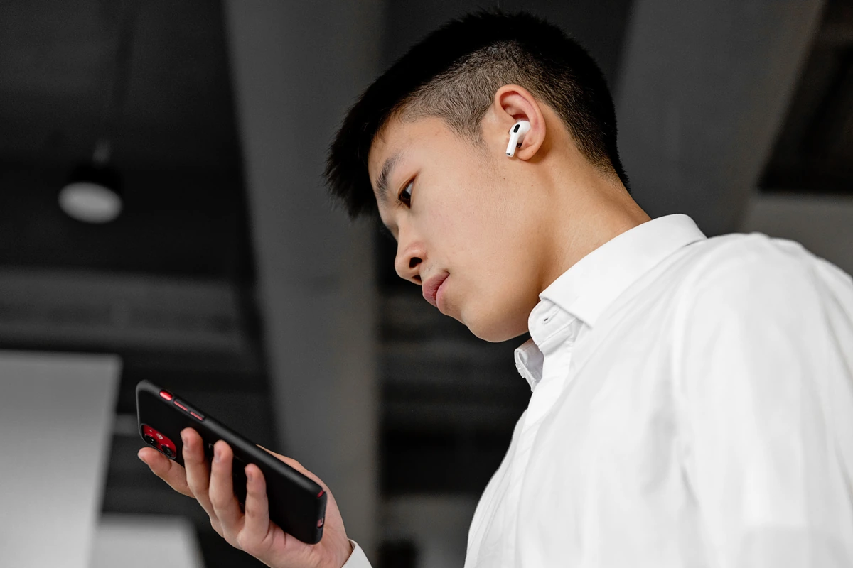 Persona mirando la pantalla de su móvil con un único auricular inalámbrico puesto en un oído