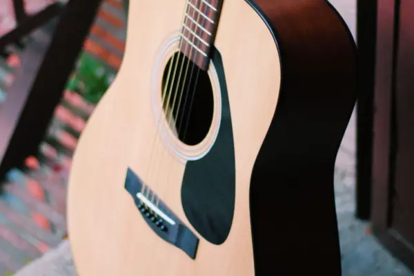 Guitarra acústica de tapa de madera natural apoyada, con la boca y el golpeador a la vista