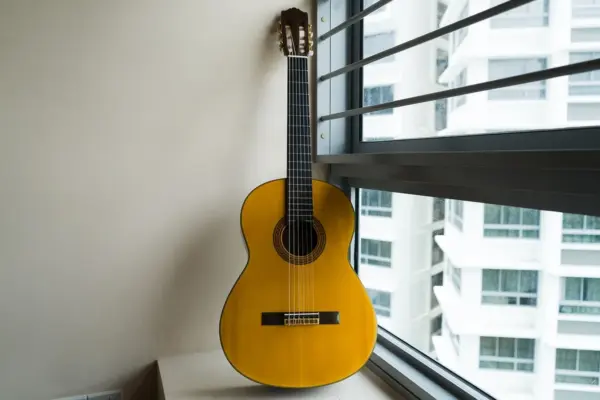 Guitarra clásica de cuerdas de nylon apoyada junto a la ventana de una habitación, con la roseta y el clavijero de palas a la vista