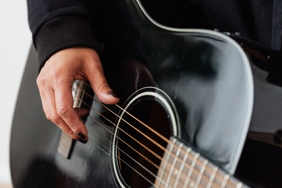 Mano pulsando las cuerdas de una guitarra acústica sobre la boca del instrumento
