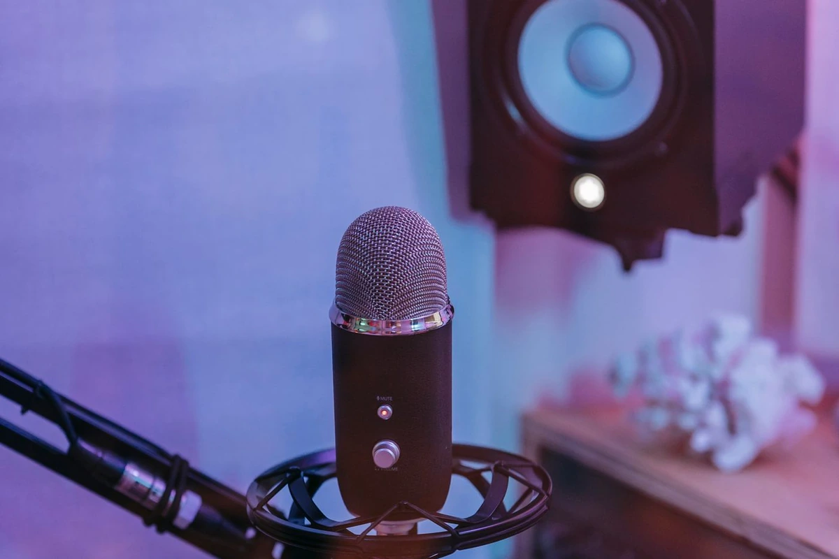 Micrófono de estudio en su soporte antivibratorio con un altavoz monitor al fondo