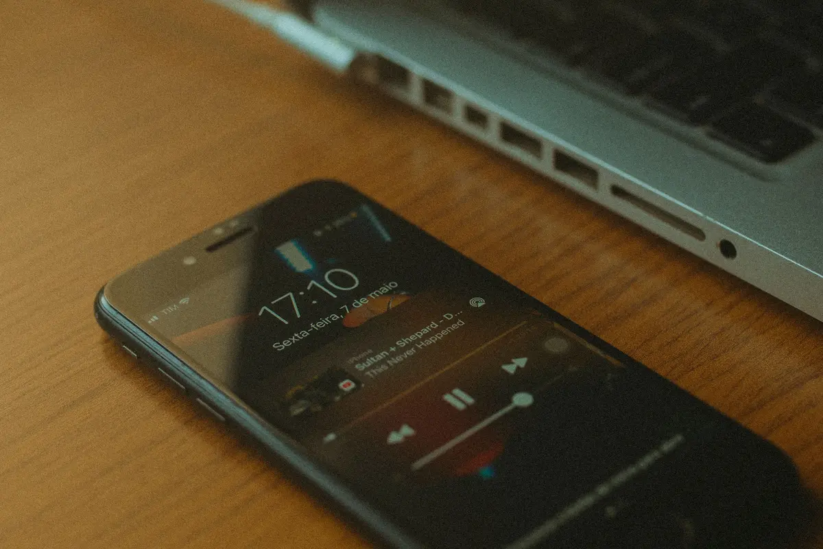 Movil reproduciendo musica sobre una mesa de madera junto a un portatil