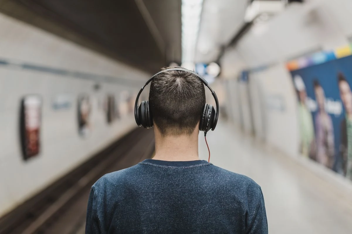 Persona de espaldas escuchando música con auriculares de diadema en el metro