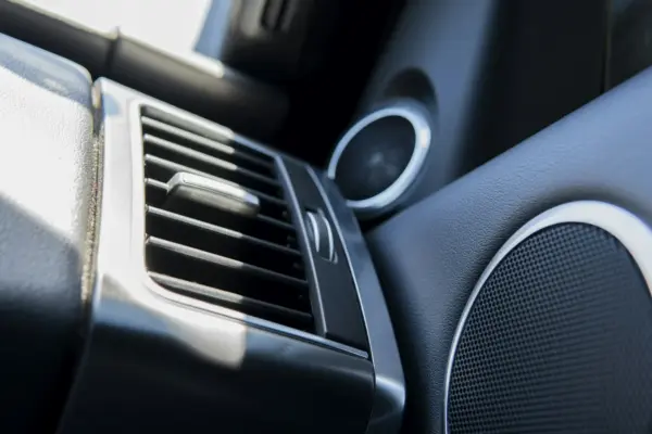 Rejilla de altavoz en la puerta interior de un coche junto al tweeter y la salida de ventilación del salpicadero, con luz natural