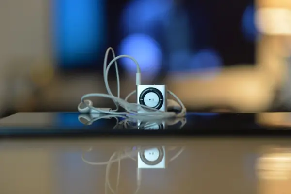 Reproductor MP3 portátil con auriculares de cable conectados sobre una mesa brillante, con el fondo desenfocado