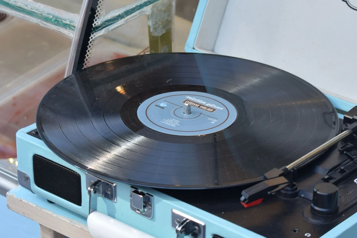 Tocadiscos portátil de tipo maleta, azul claro, con un vinilo puesto