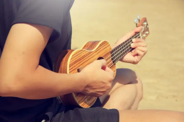 Persona tocando un ukelele de madera sentada en la playa
