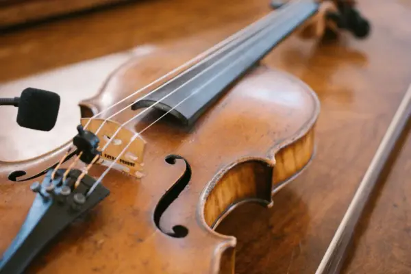 Violín de madera apoyado sobre una mesa con el puente, el cordal y las cuatro cuerdas a la vista